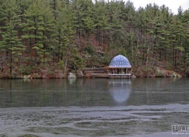 Photo of Fitchburg Reservoir - water in foreground, In rear is shore dovered with trees and a small structure.